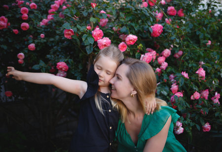 mom hugs her little daughter against the background of a rose bushの写真素材
