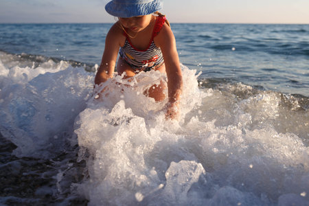 little girl in a striped swimsuit playing on the waves in the seaの写真素材