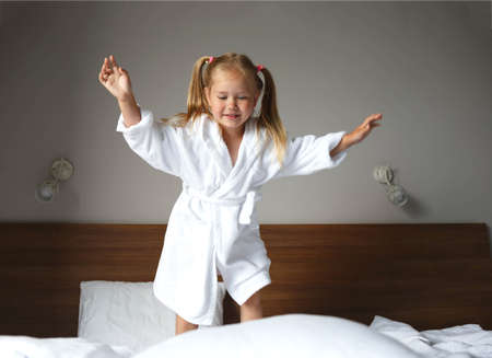 little cute girl in a white robe jumping on the bed.の写真素材
