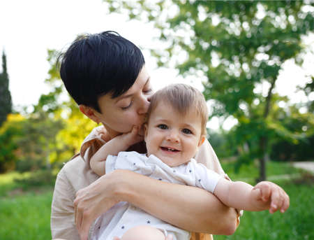 young mom kisses her little son while sitting in the park on the lawn.の写真素材
