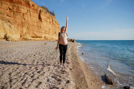 young pregnant woman with a backpack walks along the sea.の写真素材