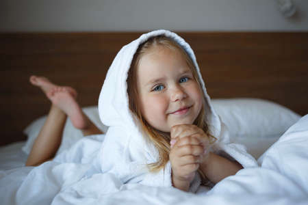 portrait of a little girl in a robe lying on the bed in the bedroomの写真素材