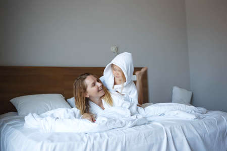 mom and daughter lie on the bed in white hotel robes after a shower.の写真素材