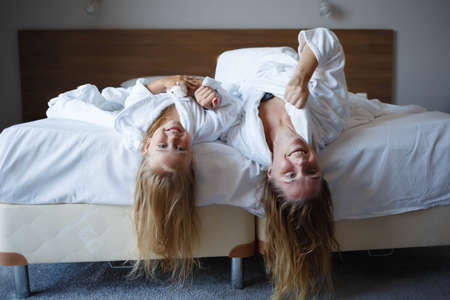 mom and daughter lie on the bed in white hotel robes after a shower.の写真素材