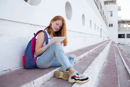 teenage girl draws in the sketchbook while sitting on the steps.