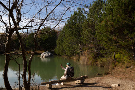 young woman hiker sits on a wooden bench by the lake in the mountains.の写真素材