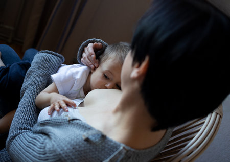 young woman breastfeeding her little son while sitting in a cozy armchair in the bedroom.の写真素材