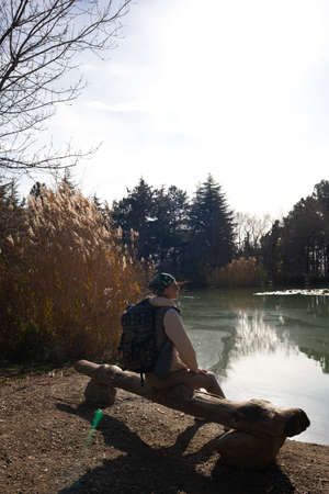 young woman hiker sits on a wooden bench by the lake in the mountains.の写真素材