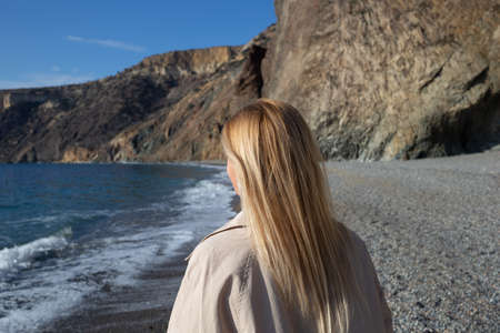 young beautiful woman on the seashore against the background of rocks.の写真素材