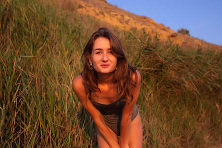 young beautiful woman in a halter swimsuit walks along the beach at sunset.の写真素材