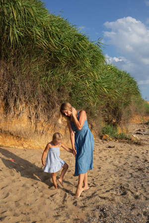 little girl walking with her mom at sunset on the beach near the sea.の写真素材