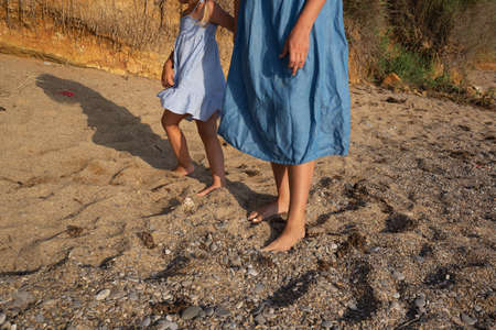 close-up shot, mother and daughter walking barefoot along the seashore