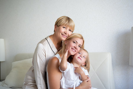 family portrait: mom, daughter and granddaughter are sitting on the bedの写真素材