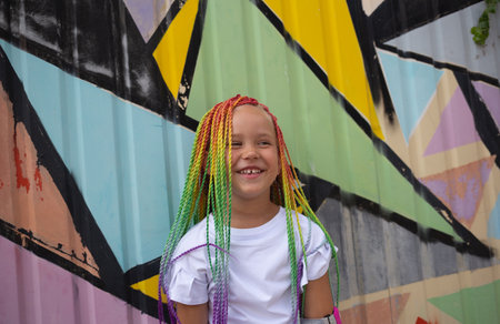 portrait of a little beautiful girl with multi-colored pigtails on the background of a colorful wall.の写真素材