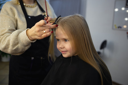 the hairdresser in the barbershop combing the hair of a little cute girlの写真素材