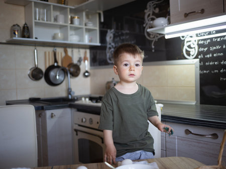 little cute boy paints eggs for easter sitting in the kitchen at the tableの写真素材