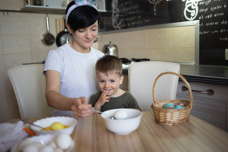little cute boy with mom paints eggs for easter sitting in the kitchen at the tableの写真素材