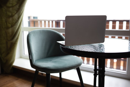 Close-up of a table with a laptop and a chair in front of a large window. remote work concept.の写真素材
