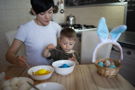 little cute boy with mom paints eggs for easter sitting in the kitchen at the tableの写真素材