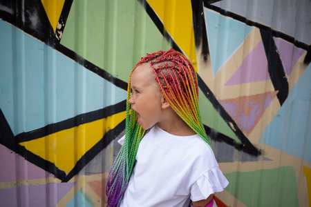 portrait of a little screaming beautiful girl with multi-colored African braids against a colorful wall.の写真素材