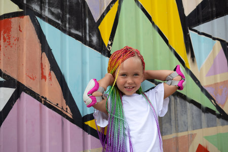 portrait of a little beautiful girl with multi-colored african braids on the background of a colorful wallの写真素材