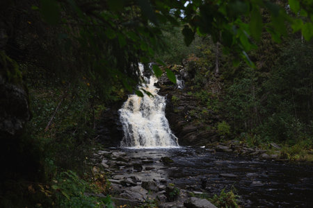 beautiful full-flowing autumn waterfall surrounded by forests and mountains.