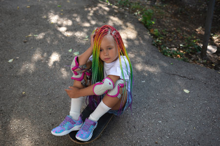 little cute girl with colorful afro pigtails sits on a skateboard.の写真素材