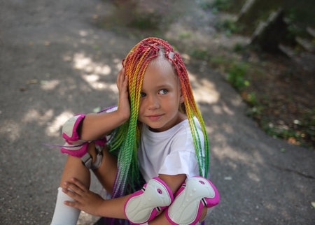 little cute girl with colorful afro pigtails sits on a skateboard.の写真素材