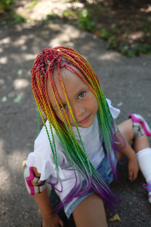 little cute girl with colorful afro pigtails sits on a skateboard.の写真素材