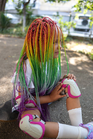 little cute girl with colorful afro pigtails sits on a skateboard.の写真素材