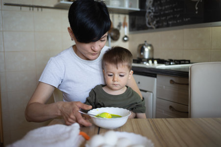 little cute boy with mom paints eggs for easter sitting in the kitchen at the tableの写真素材