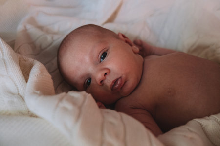 little cute newborn baby lies wrapped in a white blanket on the bed.