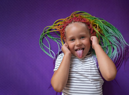 portrait of a little beautiful girl with multi-colored pigtails, lying on a purple backgroundの写真素材