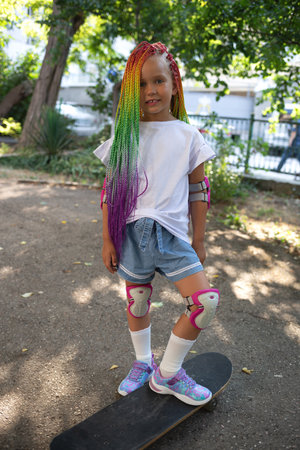 little cute girl with colorful afro pigtails standing on a skateboardの写真素材