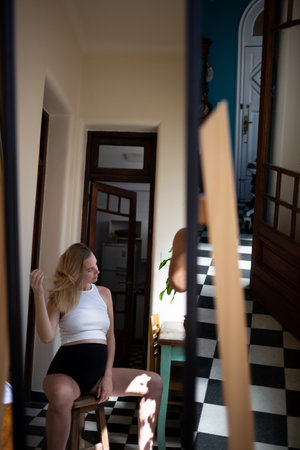 young beautiful pregnant woman looks in a large mirror while sitting in her authentic vintage apartment.の写真素材