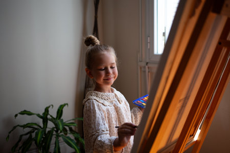 little cute girl draws with paints on canvas at the easel. the concept of early development of childrens talents.の写真素材