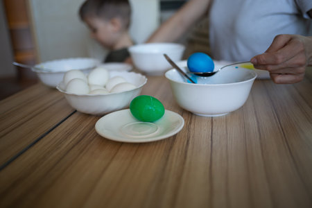 little cute boy paints eggs for easter sitting in the kitchen at the tableの写真素材