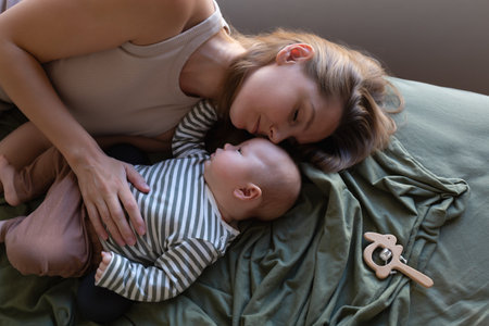 mother and newborn baby are lying on the bed in the bedroom opposite the windowの写真素材