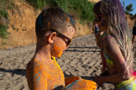 children painted with colorful holi colors have fun on the beach with their friendsの写真素材