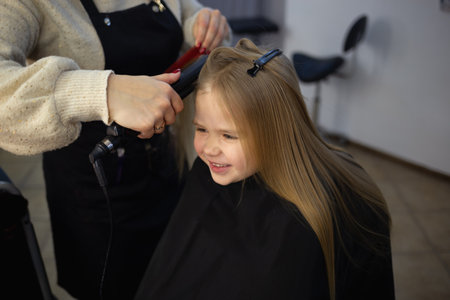 the hairdresser in the barbershop combing the hair of a little cute girl.の写真素材