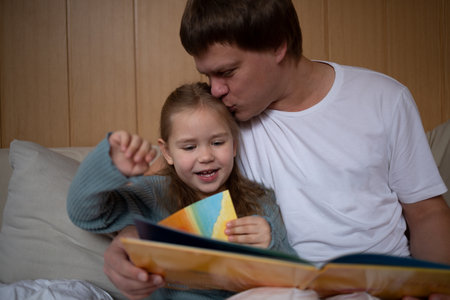 little cute girl with dad read a book sitting in the bedroom on the couchの写真素材