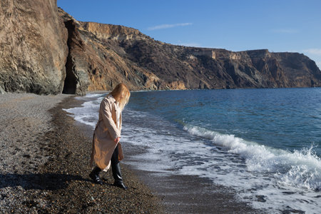 a young beautiful woman runs along a pebble beach against the backdrop of rocks and the sea.の写真素材