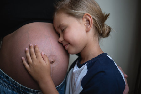 Little cute daughter hugging pregnant mother at home.の写真素材