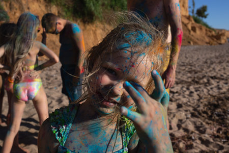 little beautiful girl painted with colorful holi colors having fun on the beachの写真素材