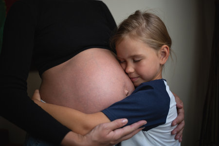 Little cute daughter hugging pregnant mother at homeの写真素材