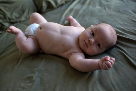 mixed race newborn baby lies wrapped in a green muslin swaddle