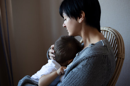 a young woman holds her little son in her arms while sitting in a cozy armchairの写真素材