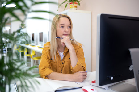 young woman sits at a computer in the office. remote work conceptの写真素材
