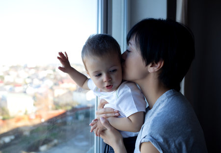 little boy with his young beautiful mother look out the window
