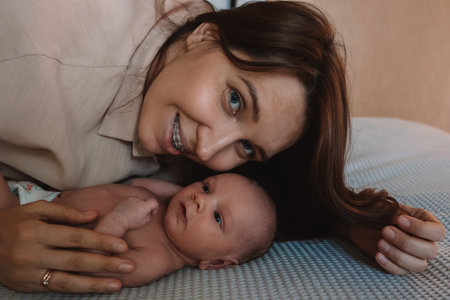 young beautiful mother kisses her newborn baby while lying on the bed in the bedroomの写真素材